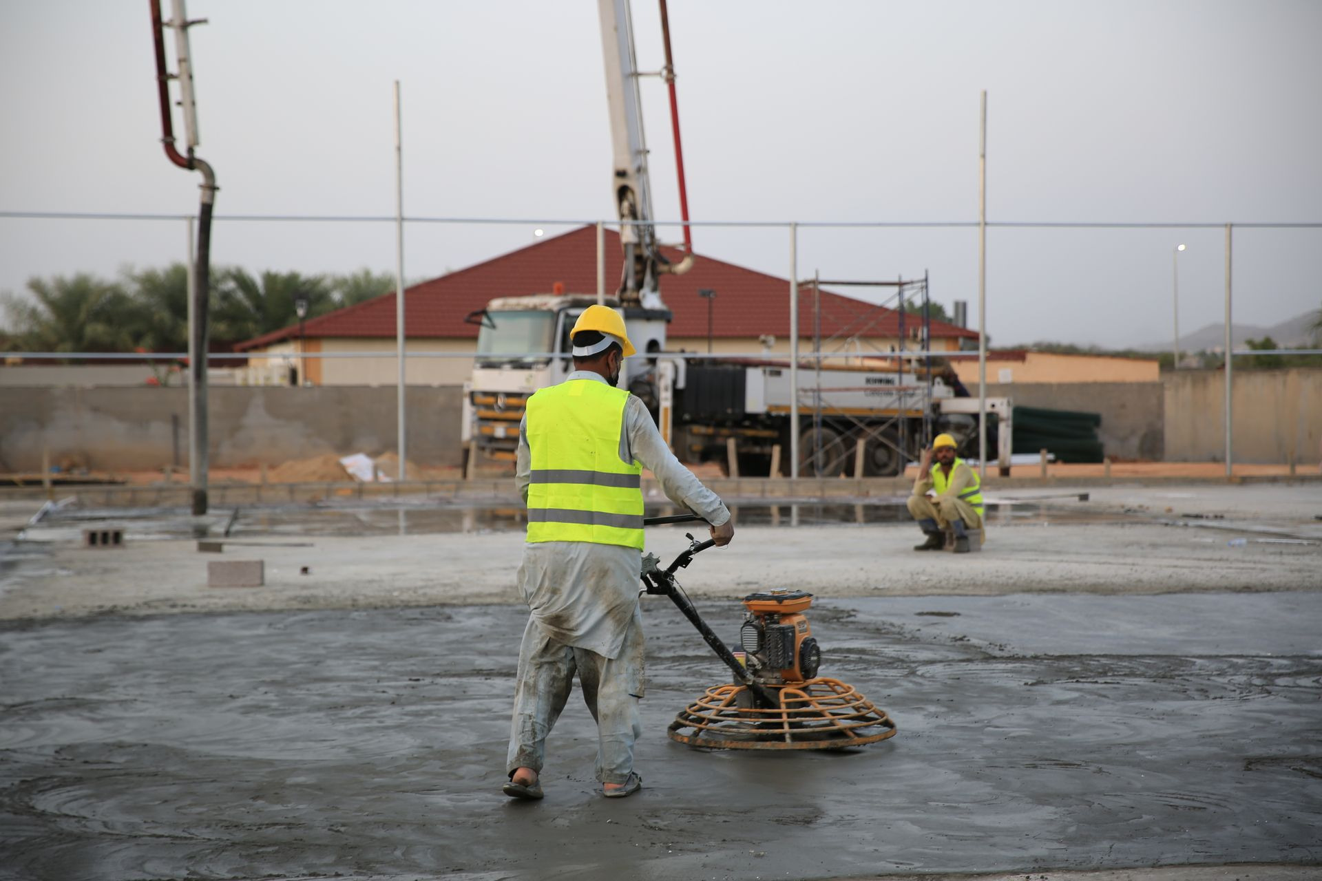 Worker running a power trowel across a large freshly poured concrete slab