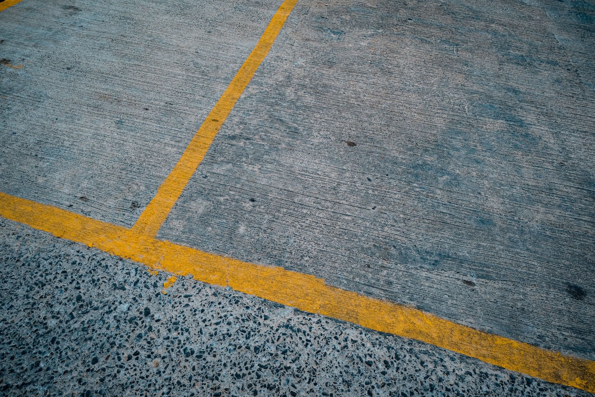 Yellow painted stall lines running across a concrete parking lot surface