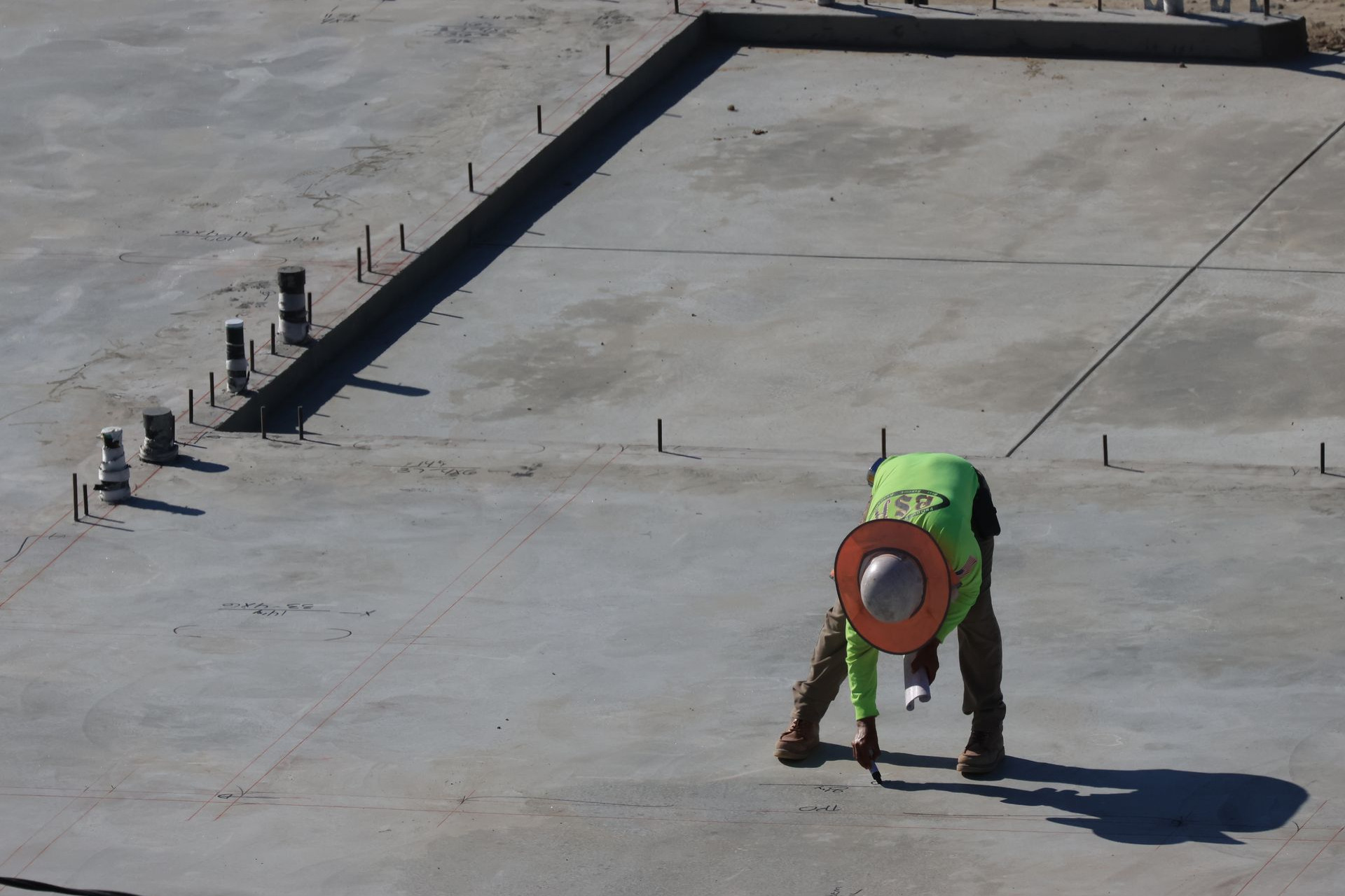 Worker marking layout lines across a large finished concrete slab with rebar dowels set along the edge