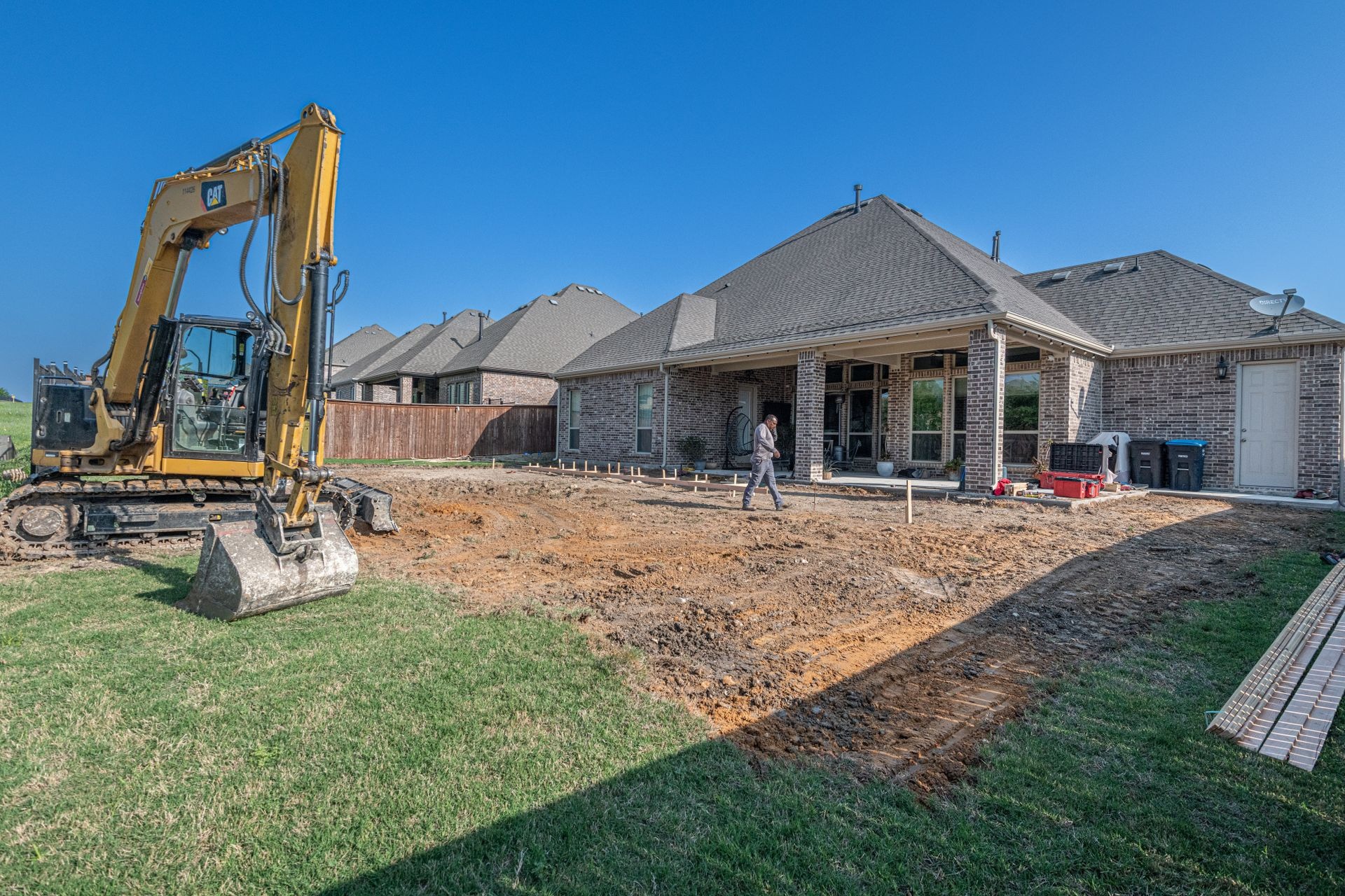 New brick home under construction with an excavator and the ground prepared for concrete flatwork