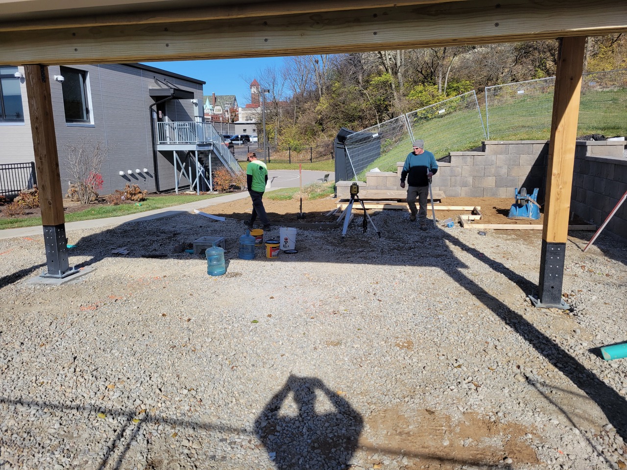 Affinity crew setting forms and checking grade with a laser level over a compacted stone base beneath a covered pavilion