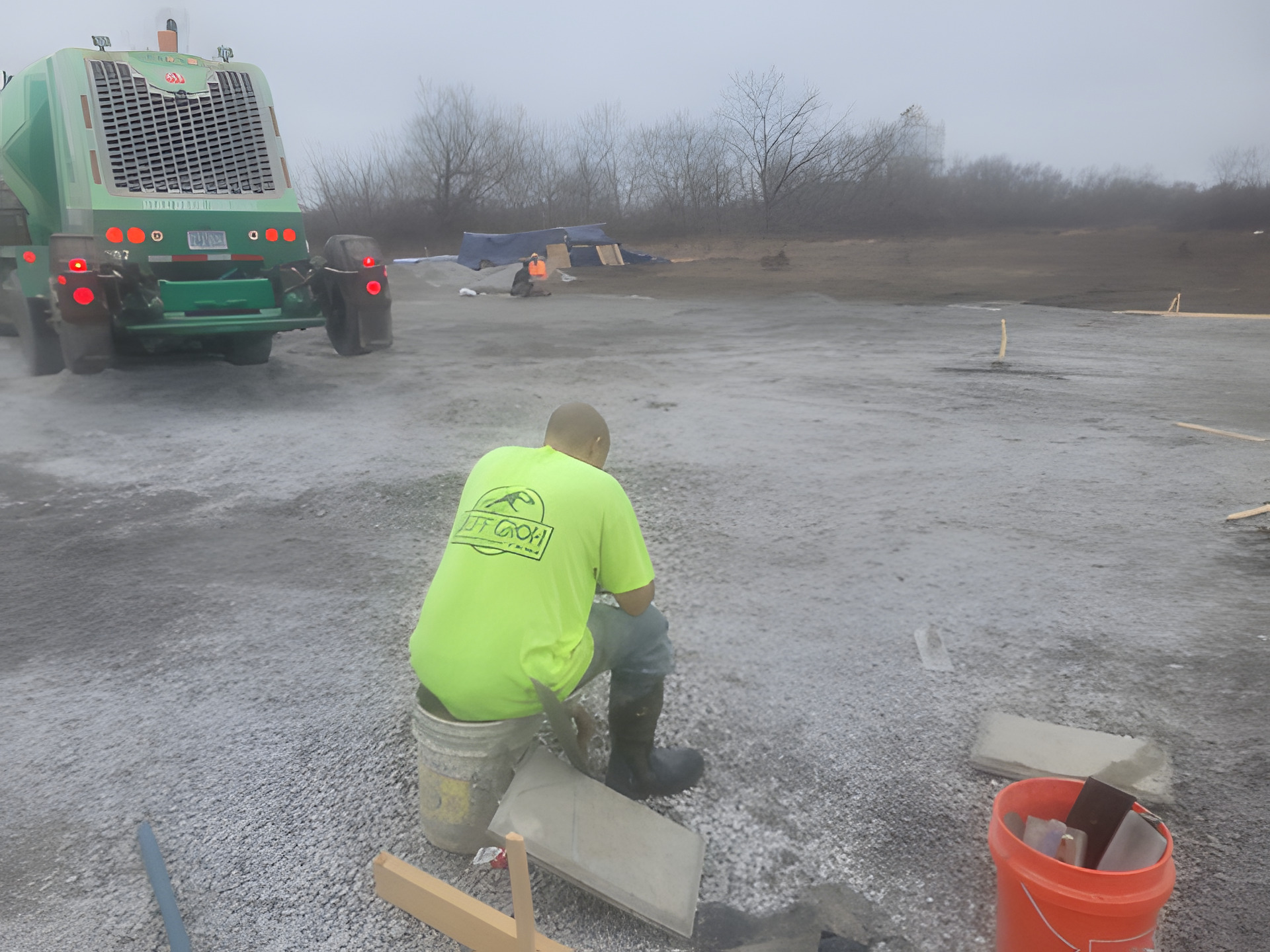 Concrete finisher working at the edge of a commercial pour with a mixer truck on the stone base behind him