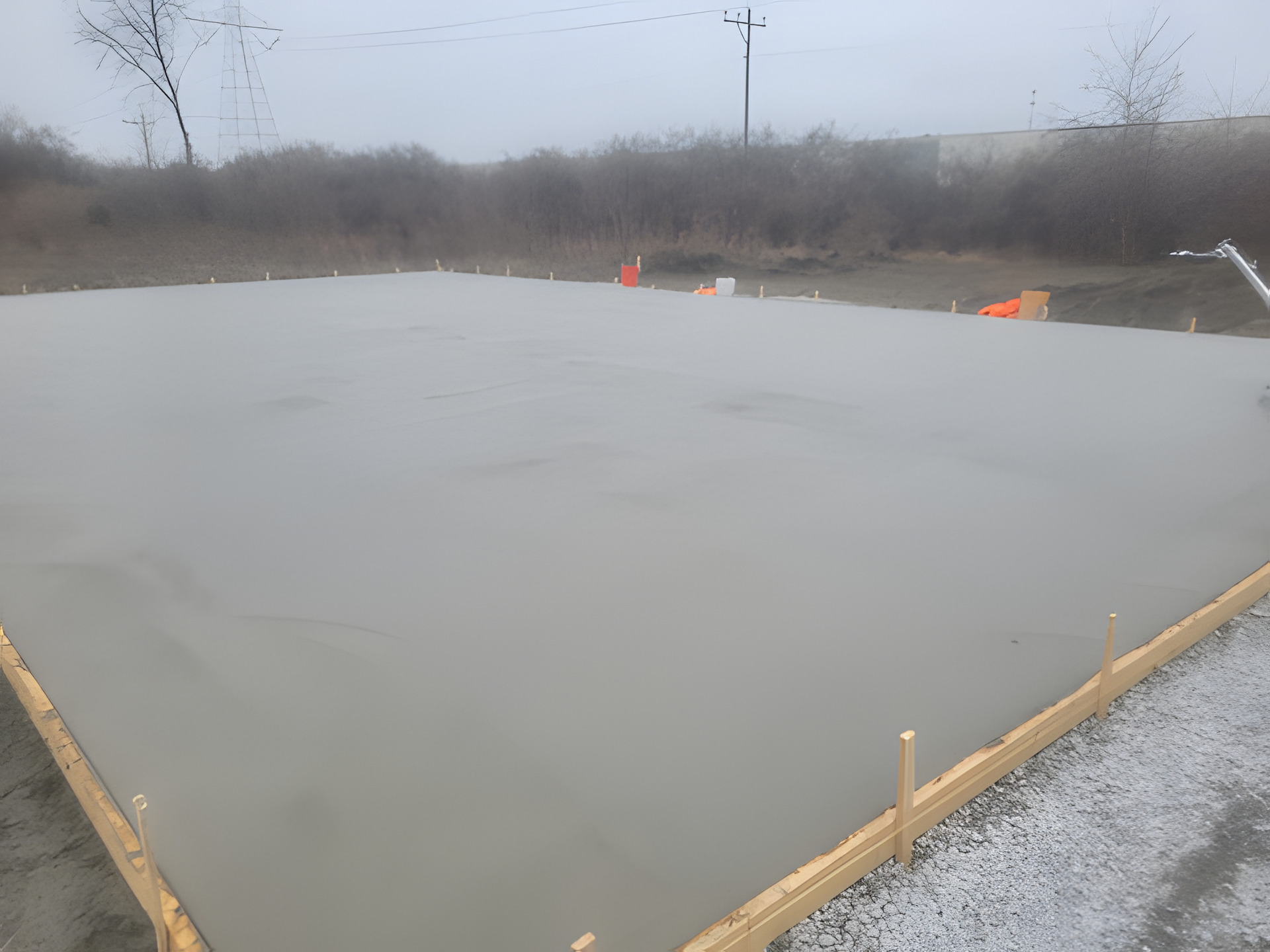 Large freshly finished concrete pad held by timber edge forms on an open commercial lot