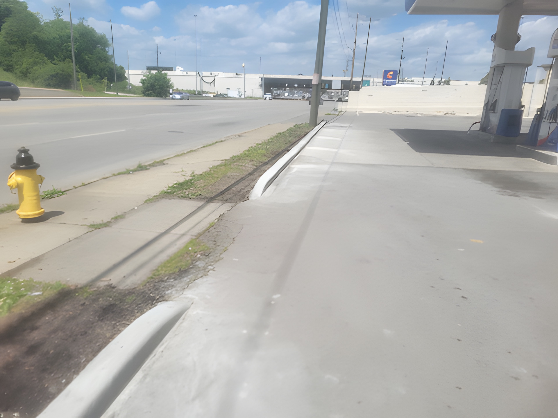 New concrete curb and entrance approach at a commercial property on a main road, next to a fire hydrant and fuel canopy