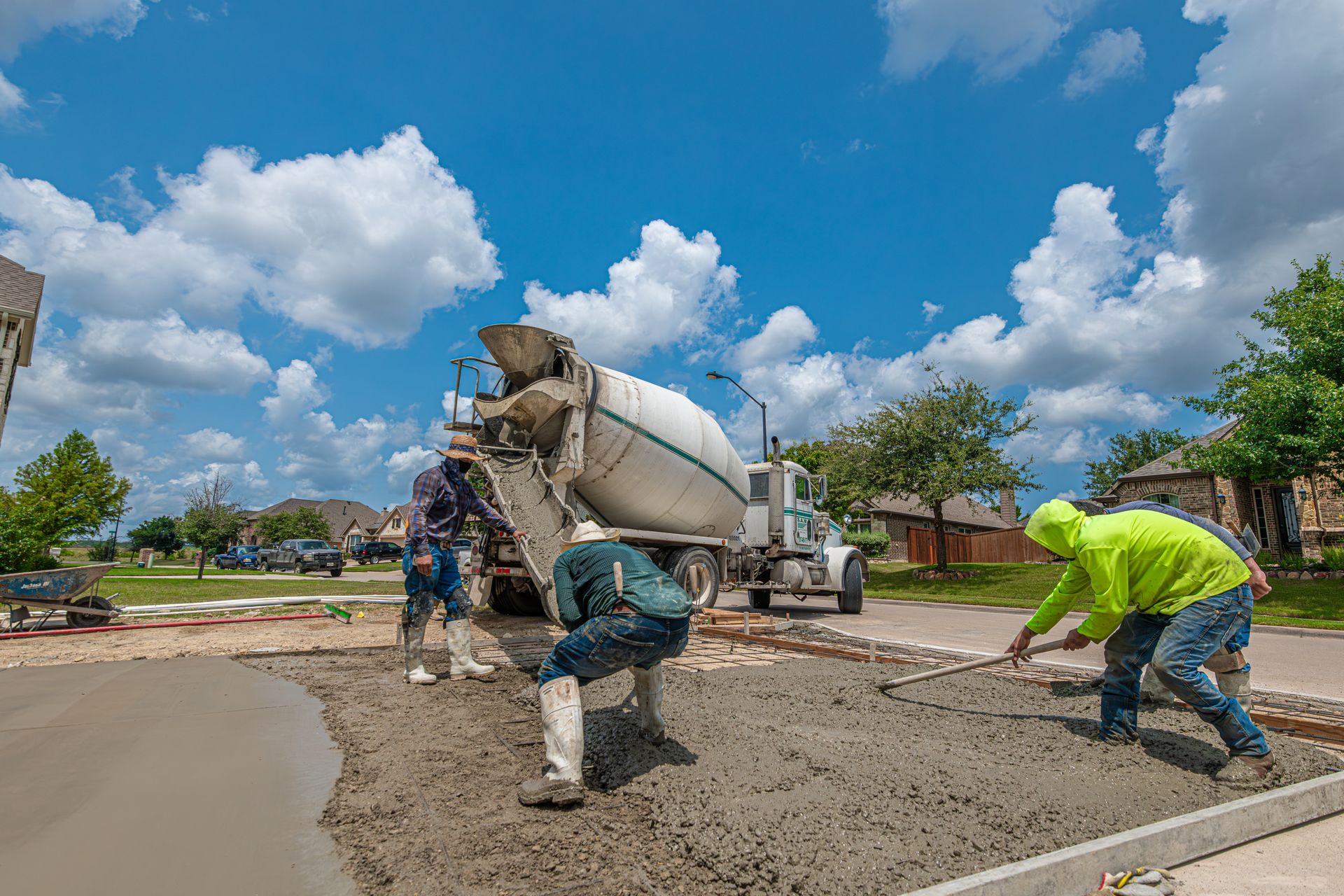 Concrete crew raking and leveling fresh concrete for a new residential driveway while a ready-mix truck unloads