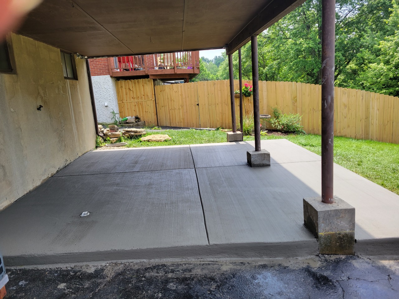Finished concrete patio slab poured beneath a raised deck in a fenced residential backyard