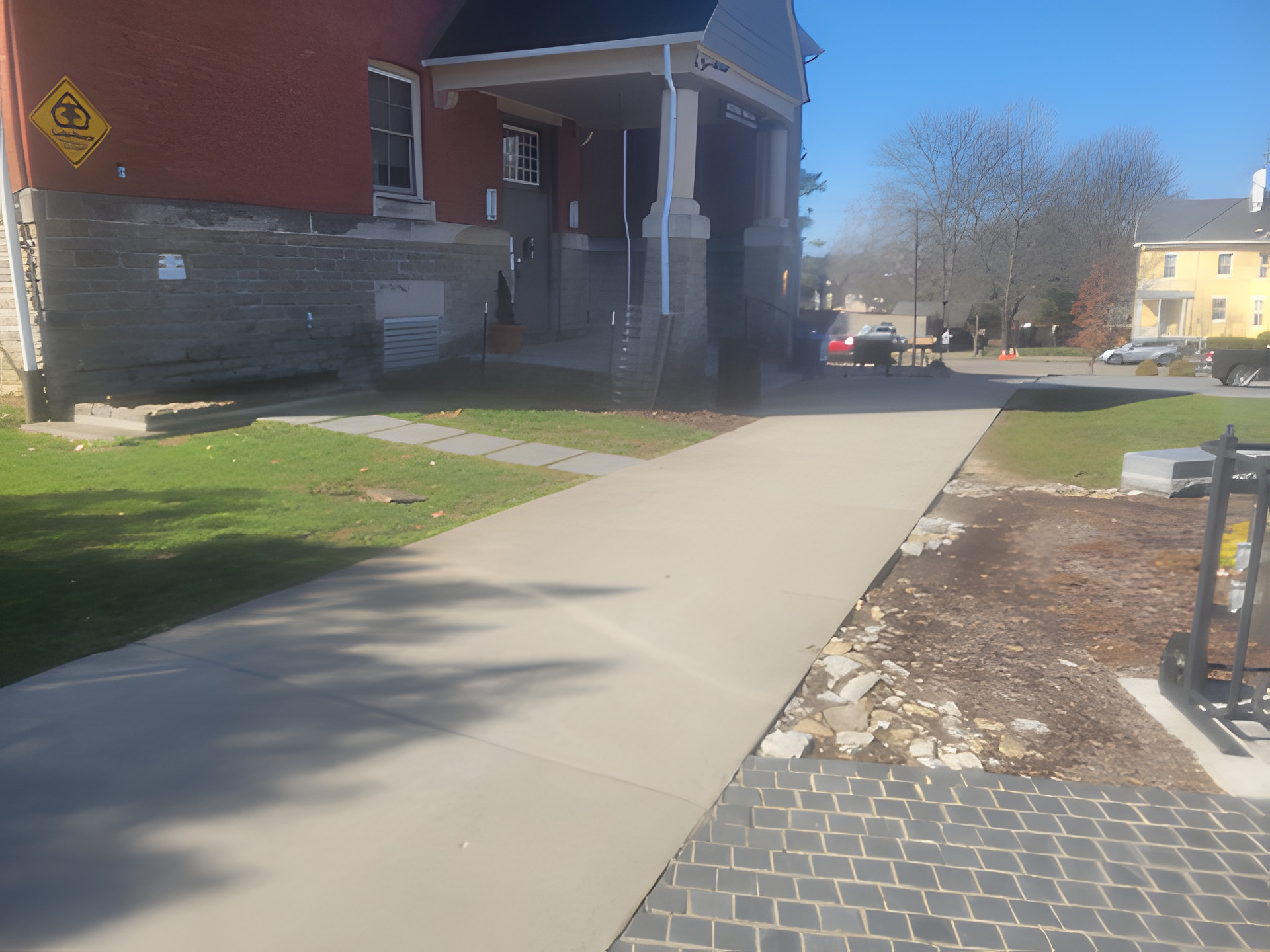 Wide concrete sidewalk running past the stone foundation and covered entry of a historic brick building