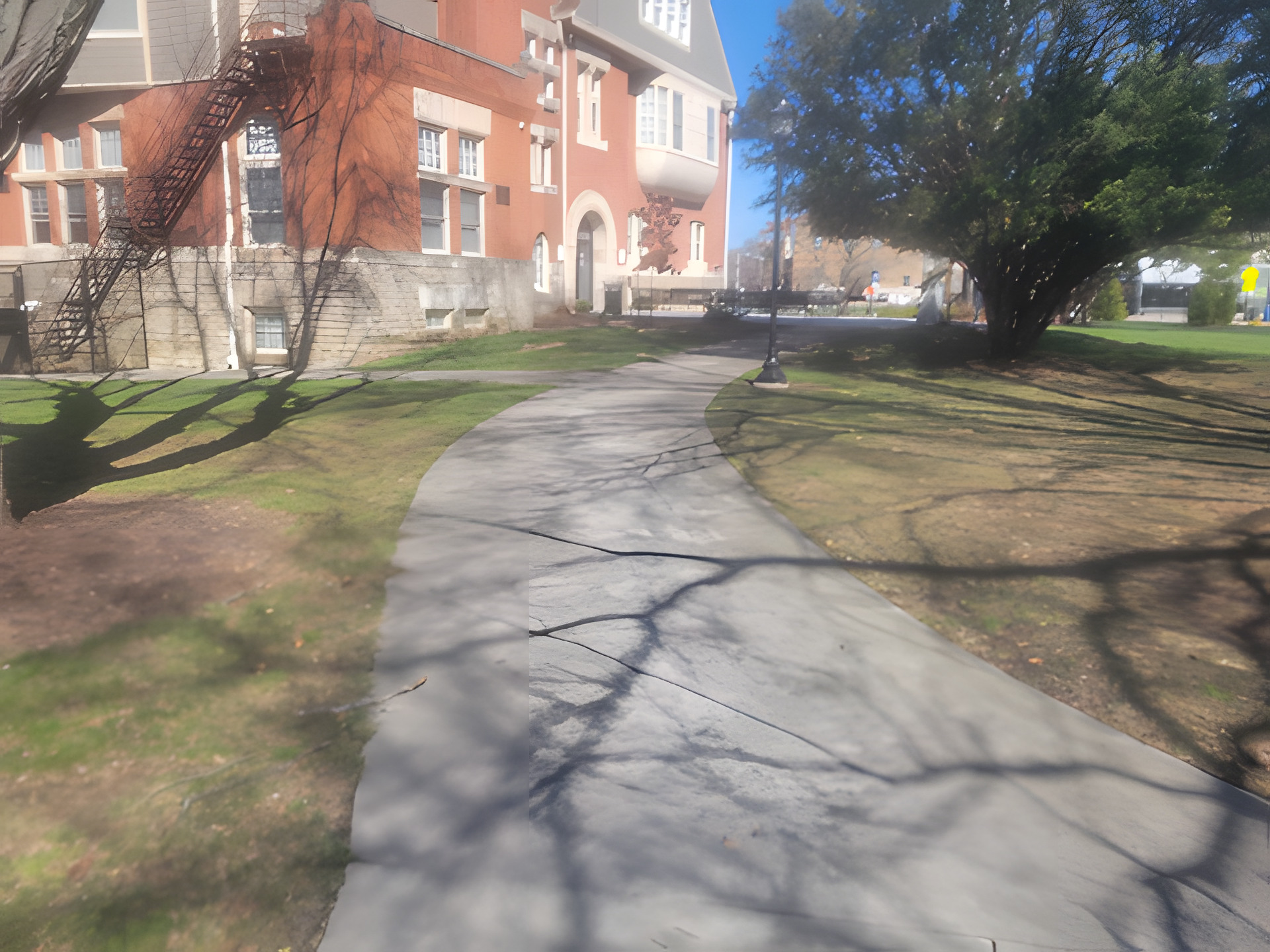Curved concrete walkway crossing a lawn toward a large brick institutional building